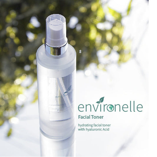 A spray bottle of Environelle Facial Toner with Hyaluronic Acid, outdoor setting with foliage in the background.