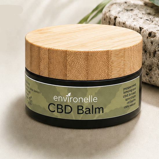 A product information card for Environelle CBD Balm, featuring a photo of a wooden balm container with a green label, set against a light beige background with text detailing its natural ingredients and benefits.